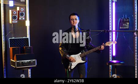 Donna rocker vestita in pelle esegue uno spettacolo dal vivo con melodie heavy metal e performance vocale per gli amanti della musica. Un cantante ribelle e audace suona la chitarra con una presenza sul palco selvaggia. Telecamera B.. Foto Stock