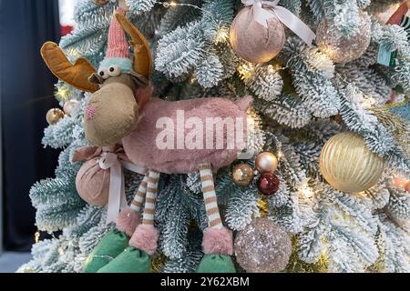 Giocattolo per l'albero di Natale sotto forma di renna divertente e palle dorate sui rami innevati dell'albero di Natale. Sfondo natalizio. Foto Stock