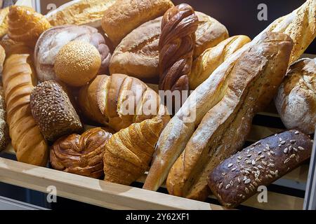 Un bancone da forno con una vasta gamma di panini, panini e baguette. Un'illuminazione calda e luminosa mette in risalto la freschezza. Foto Stock