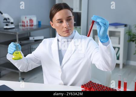 Analisi di laboratorio. Medico con il campione di sangue nella provetta e nella beuta al tavolo all'interno Foto Stock