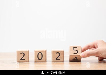 Una mano cambia il blocco da 2024 a 2025 su un tavolo di legno, simboleggiando l'approccio del nuovo anno Foto Stock