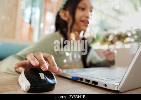 Adolescente asiatica sorridente mentre comunica con un amico tramite Internet utilizzando il portatile in un ristorante Foto Stock