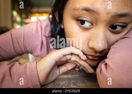 Asiatico adolescente ragazza in un cattivo umore giacendo il suo corpo e mettendo le sue braccia su tavolo Foto Stock