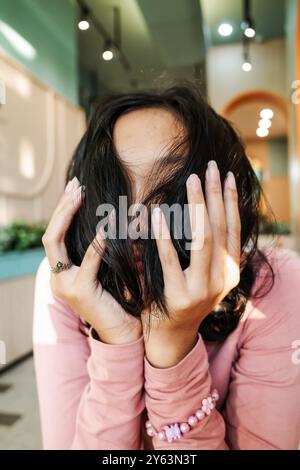 Adolescente asiatica che regge il mento sulle mani e copre il viso con i capelli Foto Stock