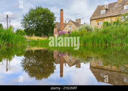 Vecchia torre in mattoni e edifici in pietra che si riflettono in un fiume calmo fiancheggiato da vegetazione verde nel macello inferiore. Foto Stock