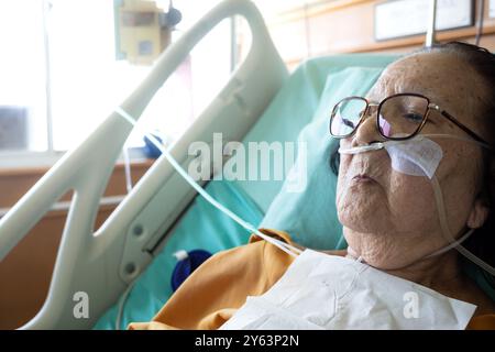 Donna anziana asiatica malata che si trova nel letto d'ospedale sottoposto a trattamento ospedaliero che indossa un tubo di ossigeno Foto Stock