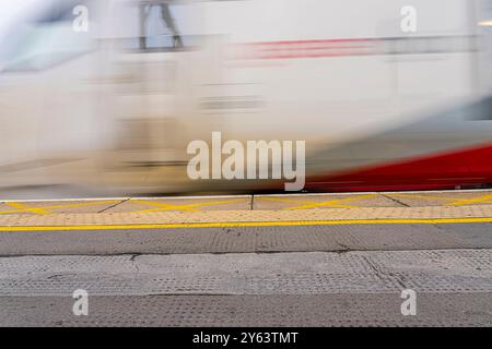 Marcatura gialla del bordo sulla piattaforma ferroviaria di superficie con effetto sfocato del treno in velocità. Foto Stock