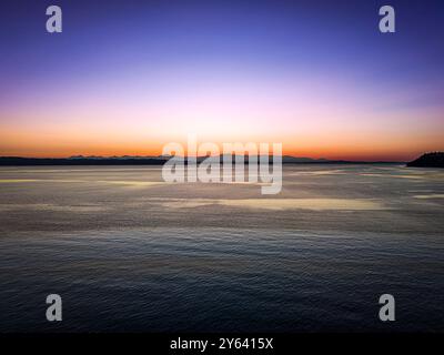 Uno splendido tramonto su un mare calmo con un cielo in pendenza che passa dall'arancione al blu. Foto Stock