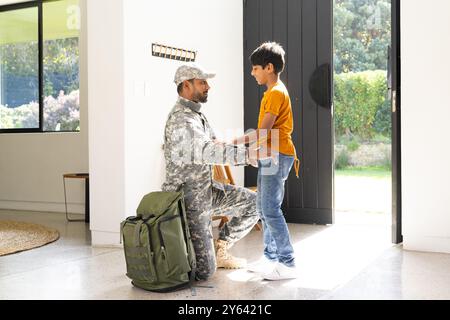 Accogliente casa, giovane figlio che abbraccia il padre indiano in uniforme militare alla porta Foto Stock