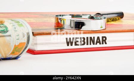 Parole DEL WEBINAR scritte alla fine del libro su uno sfondo bianco in una composizione con lente d'ingrandimento e banconote in dollari americani Foto Stock