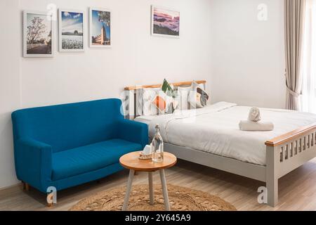 Interni eleganti di una camera da letto moderna. Accogliente camera interna con letto, divano e tavolo blu. Arredi per la casa. Interno con letto king size e biancheria da letto bianca. Intelligenza artificiale Foto Stock