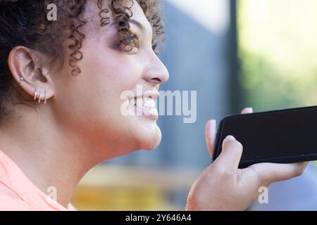 Donna sorridente che tiene in mano lo smartphone e registra messaggi vocali durante le attività all'aperto, a casa Foto Stock