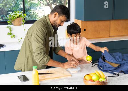 Pranzo al sacco, padre e figlio indiani che mettono cibo e frutta nello zaino della scuola Foto Stock