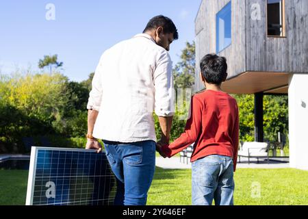 padre e figlio indiani che trasportano pannelli solari, camminano insieme nel cortile Foto Stock