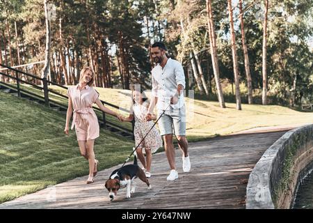 Giornata di famiglia. Intera famiglia di tre persone che si tengono per mano e sorridono mentre cammina nel parco Foto Stock