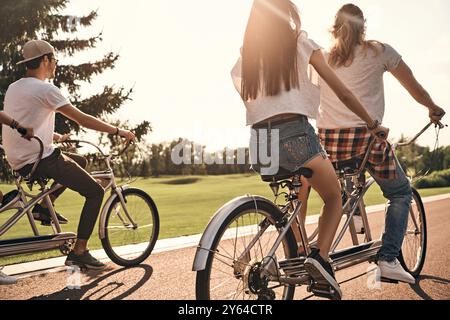 La vita è migliore con gli amici. Gruppo di giovani che praticano abbigliamento casual che vanno in bicicletta insieme mentre trascorrono del tempo libero all'aperto Foto Stock