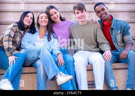 Adolescenti sorridenti seduti sulle scale che si abbracciano guardando la macchina fotografica Foto Stock