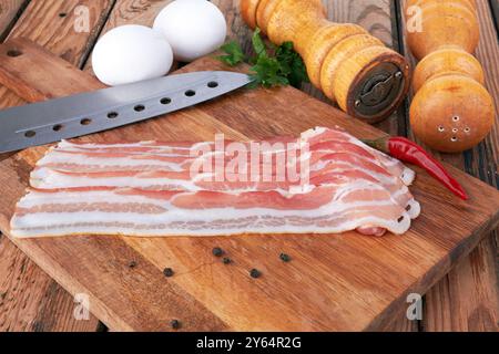 Pancetta su un tagliere con pepe caldo e uova di pollo Foto Stock
