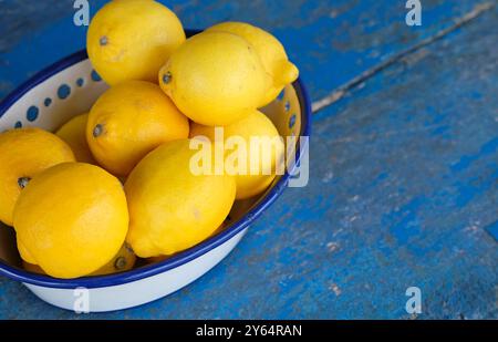 limoni gialli in una ciotola di metallo bianco su un tavolo dipinto di blu Foto Stock