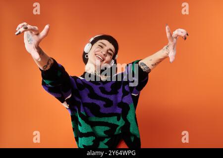 Una giovane donna animata sfoggia i suoi tatuaggi indossando un maglione colorato che irradia energia in studio. Foto Stock