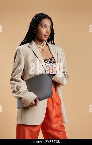 Una giovane donna trasuda fiducia nell'abbigliamento alla moda mentre tiene in mano un notebook, pronto per l'avventura. Foto Stock