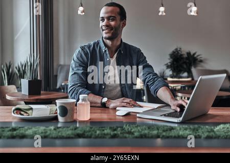 Il posto migliore per lavorare. Bel giovane che usa il computer e sorride mentre si siede al bar Foto Stock