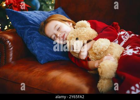 Piccola ragazza dorme vicino accesa albero di natale Foto Stock