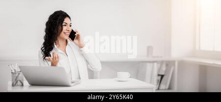 Sorridente ragazza ispanica che parla al telefono in ufficio Foto Stock
