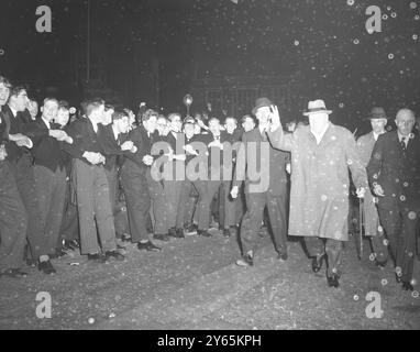 Harrows Distinguished' Old Boy gli alti scolari legano le braccia per trattenere i compagni entusiasti come il primo ministro Sir Winston Churchill dà il suo segno di " Vittoria " durante la sua visita annuale ad Harrow , la sua vecchia scuola . Sir Winston si unì alla canzone annuale nella sala del discorso. 12 novembre 1954 Foto Stock