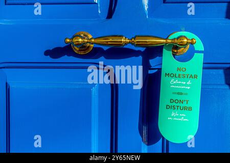 Una suggestiva porta blu con una lussuosa maniglia dorata presenta un cartello bilingue "Do Not Disturb", indicativo di una tranquilla villa di vacanza a Ibiza Foto Stock
