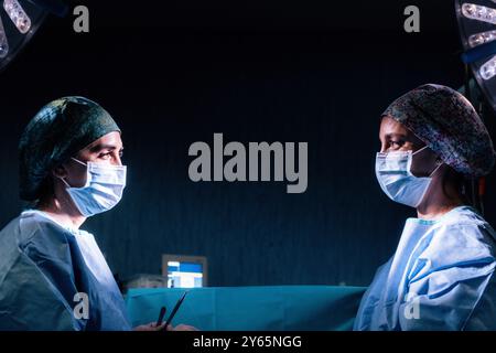 Due chirurghi femminili si trovano faccia a faccia in una sala operatoria poco illuminata, discutendo di strategia prima di un intervento chirurgico entrambi i professionisti sono in scrub, indossando S. Foto Stock