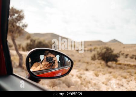 Donna irriconoscibile che cattura il paesaggio desertico di Cabo de Gata, in Spagna, utilizzando una fotocamera riflessa nello specchio laterale di un'auto. Foto Stock