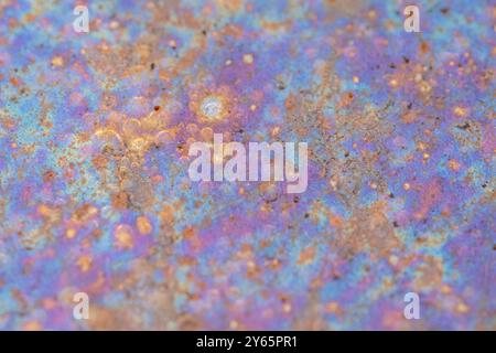 Uno scatto ravvicinato che cattura i colori vivaci e le texture intricate riflesse in una piccola pozzanghera, mostrando un'armoniosa miscela di ruggine, blu e viola Foto Stock