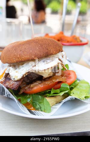 Un delizioso hamburger gourmet con succulente polpa di manzo condita con pancetta croccante, un uovo perfettamente fritto, lattuga fresca, fette di pomodoro mature e vi Foto Stock