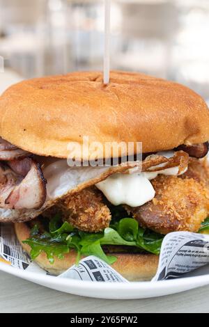 Un gustoso hamburger gourmet con una succosa polpa, pancetta croccante, un uovo fritto, rucola fresca e salsa cremosa, tutto inserito tra un panino tostato Foto Stock