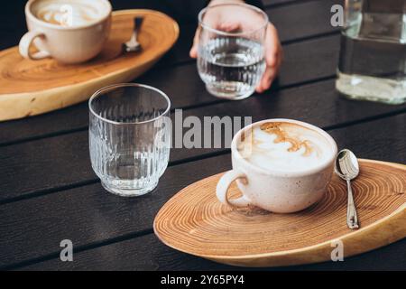 Vista dall'alto di un ambiente accogliente per la colazione, con cappuccino dal design cremoso in schiuma, servito in una tazza macchiata su un vassoio di legno accanto a un bicchiere trasparente Foto Stock