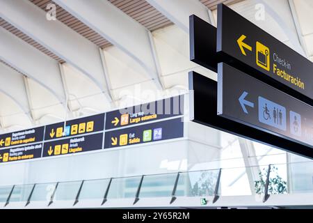 Un'immagine chiara di segnali informativi in un terminal aeroportuale che indirizzano i passeggeri verso vari impianti, tra cui check-in, ritiro bagagli e uscite, Foto Stock