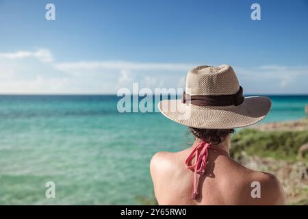 Vista posteriore di una donna irriconoscibile che indossa un cappello di paglia, rilassandosi presso la pittoresca spiaggia di Varadero a Cuba. Le acque turchesi del Mar dei Caraibi Foto Stock