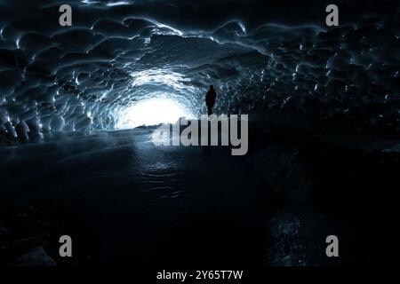 Una grotta di ghiaccio caverna illuminata da luce naturale che mostra intricati schemi di ghiaccio con una figura solitaria in piedi, creando un'affascinante e misteriosa Foto Stock