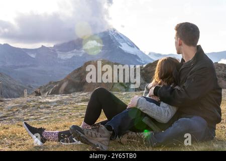 Un uomo e una donna siedono a stretto contatto in un ambiente montuoso, affacciato su una vetta maestosa, trasmettendo un momento di tranquillità Foto Stock