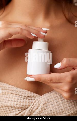 Primo piano delle mani di una giovane donna che applica un prodotto per la cura della pelle da un dispenser bianco, favorendo un regime di bellezza quotidiano Foto Stock
