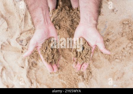 Dall'alto immagine ravvicinata di un maschio corto e irriconoscibile, due mani chiuse e che tengono la sabbia. Foto Stock