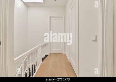 Questa immagine mostra un interno moderno e ben illuminato caratterizzato da un corridoio elegante con pavimento in legno e pareti bianche. Foto Stock