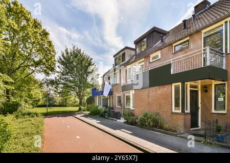 Una giornata di sole in una tranquilla strada suburbana caratterizzata da case in mattoni a due piani con balconi e lussureggianti alberi verdi. Foto Stock