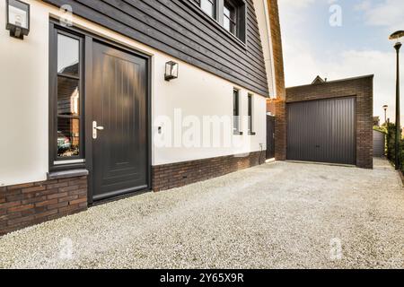 Una facciata di casa contemporanea con una porta frontale nera, rivestita in materiali misti con legno e mattoni, completata da un vialetto di ghiaia che conduce Foto Stock