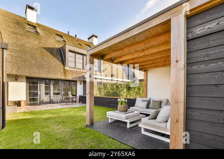 Una casa contemporanea caratterizzata da un tetto in paglia e un rilassante patio con giardino con mobili confortevoli e prato ben tenuto. Foto Stock