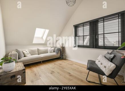 Un luminoso ed elegante soggiorno attico con un comodo divano, pavimenti in legno duro e grandi finestre con persiane. Foto Stock
