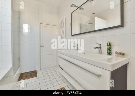 Un bagno moderno pulito e luminoso con piastrelle bianche, uno specchio e finiture contemporanee. Foto Stock