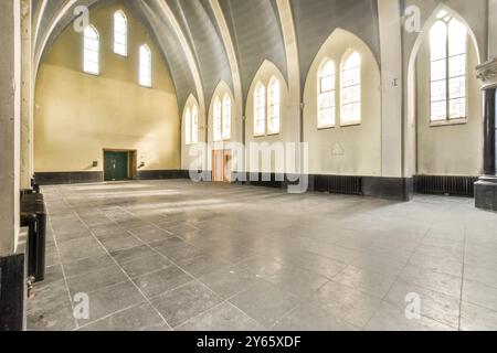 Ampia vista interna di un vecchio edificio della chiesa, con alte finestre ad arco e un pavimento vuoto, che trasuda un'atmosfera storica. Foto Stock