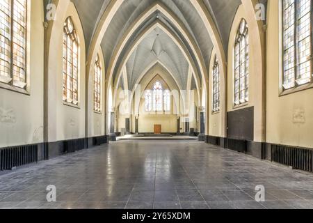 Un interno vuoto di una chiesa gotica con soffitti a volta, vetrate colorate e pavimento piastrellato nero che riflette la luce del sole. Foto Stock